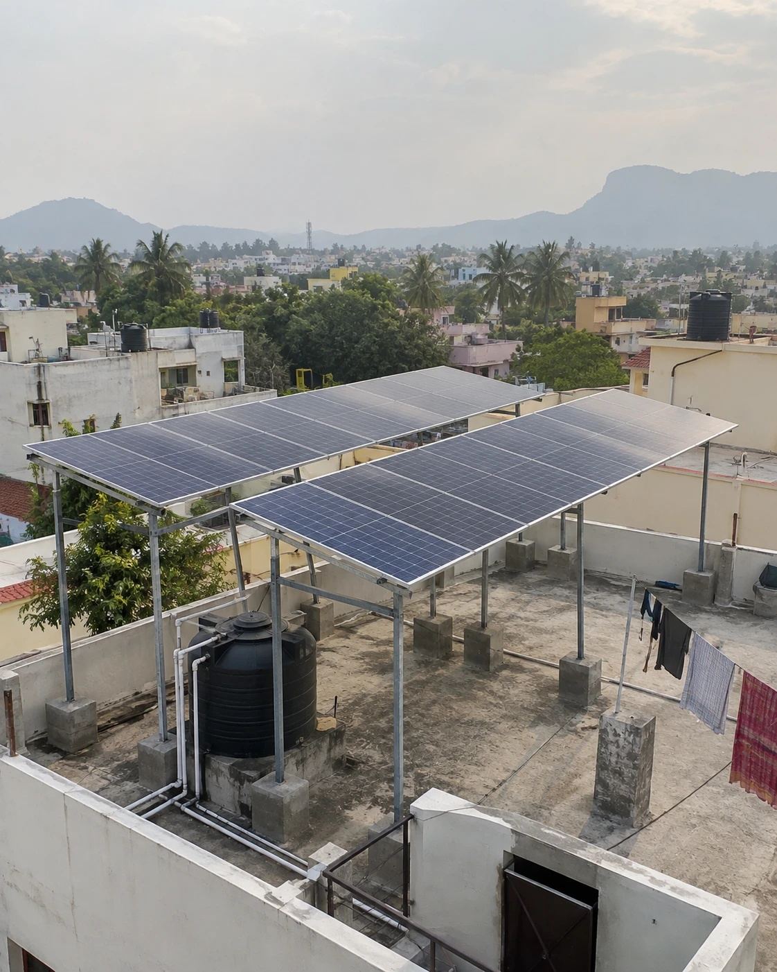 Rooftop solar panels on a raised steel structure, with a water tank and the Tirupati hills in the background